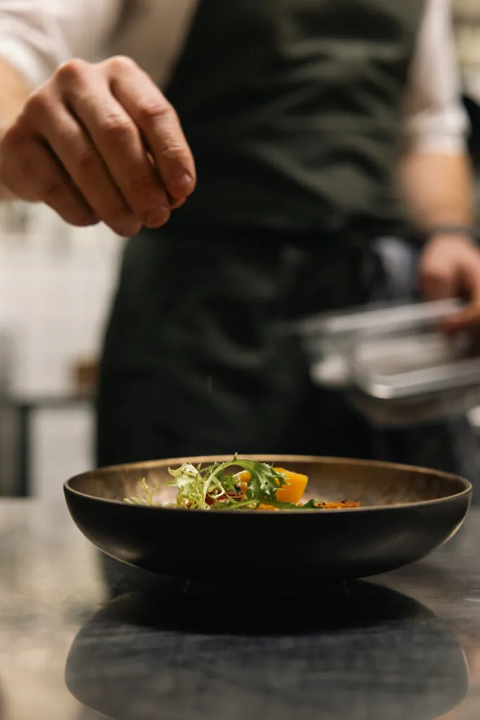 Kock förbereder elegant tallrik med färska grönsaker i restaurangkök med naturligt ljus