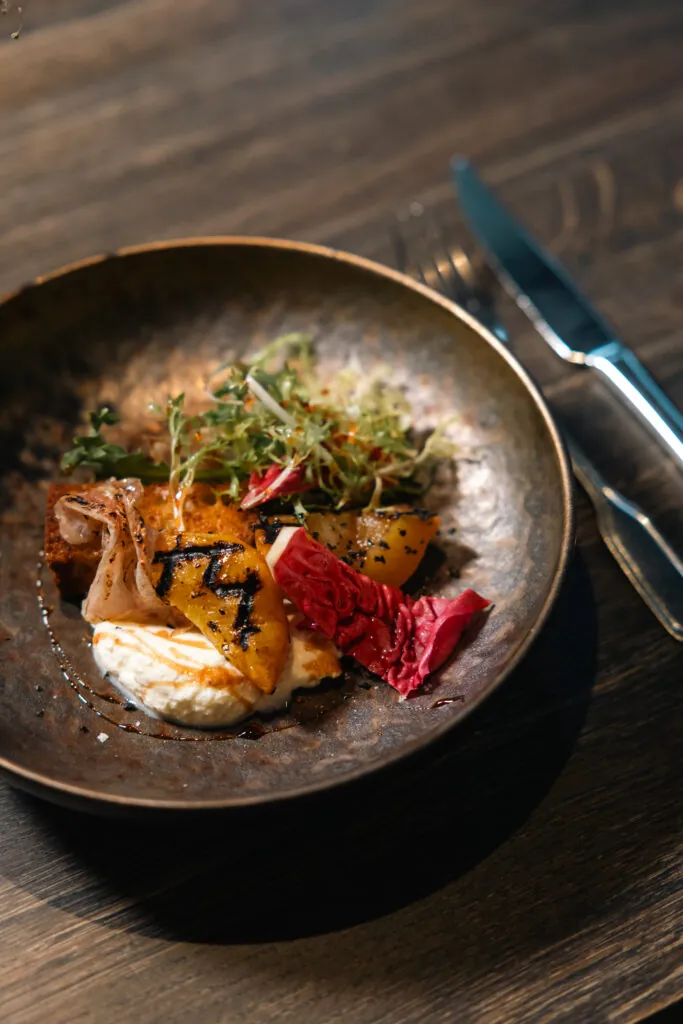 Elegant tallrik med grillad fisk, rostade grönsaker och färska örter serverad i restaurangens konstnärligt presenterad...