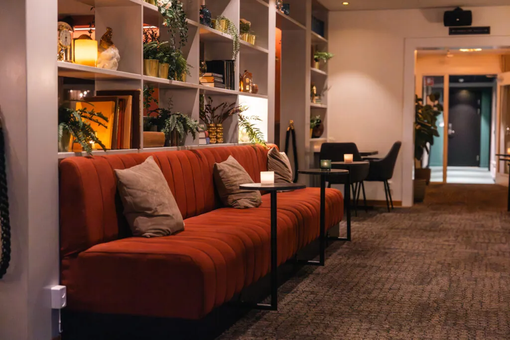 Elegant lounge med orange sammetssoffa och bokhyllor i hotellets lobby, inbjudande atmosfär för avkoppling