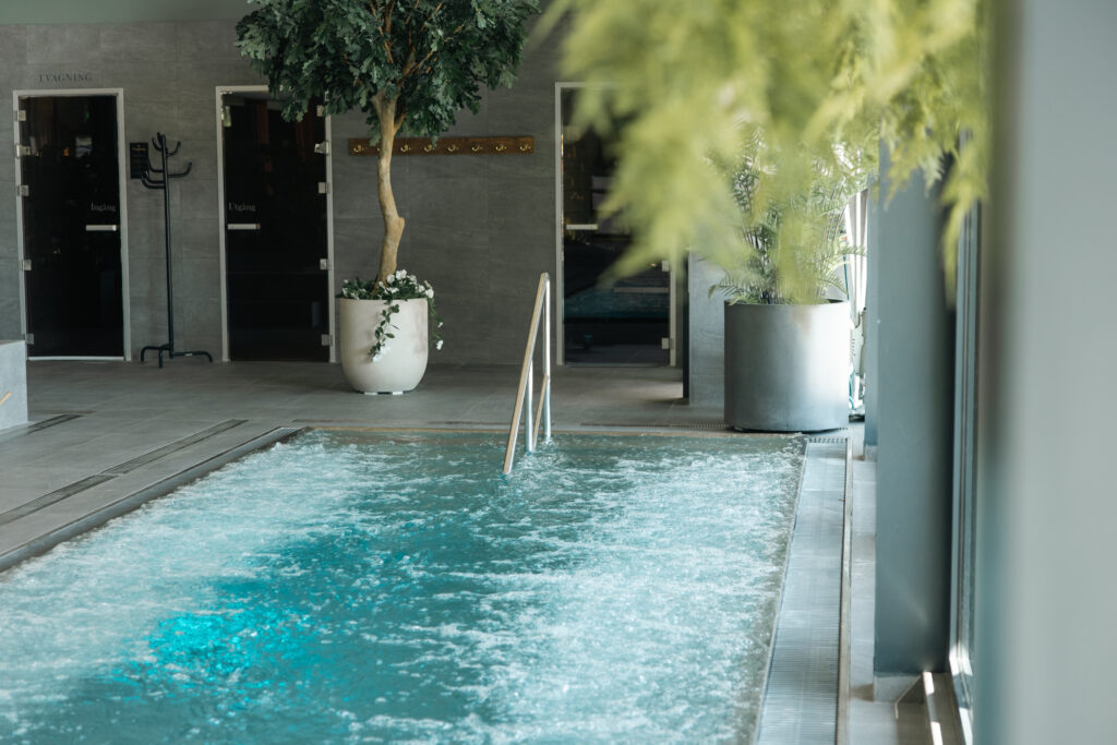 Bubblande relaxpool med handräcke omgiven av växter och spa-faciliteter med glasdörrar i modern miljö