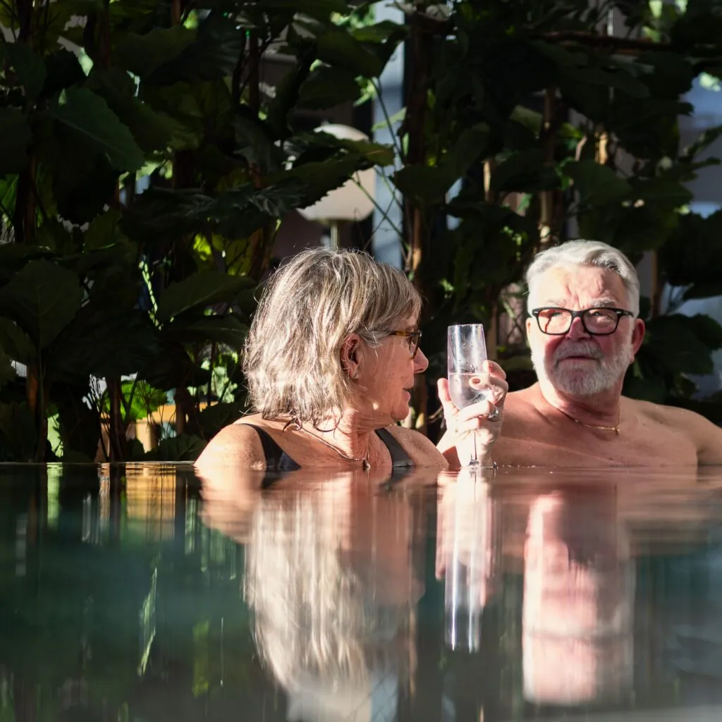 Par njuter av poolen med ett glas bubbel på Starby Spa & Hotell, omgivna av frodig grönska.