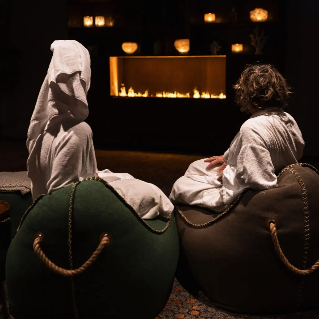 Två gäster i badrockar sitter i mjuka fåtöljer och njuter av sprossbrasan i Starby Spas avkopplingslounge