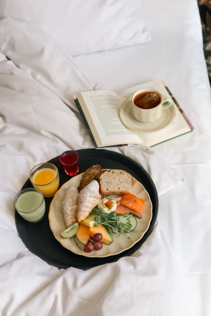 Lyxig frukost på sängen med croissanter, lax, frukt och kaffe bredvid öppen bok - perfekt för avkoppling