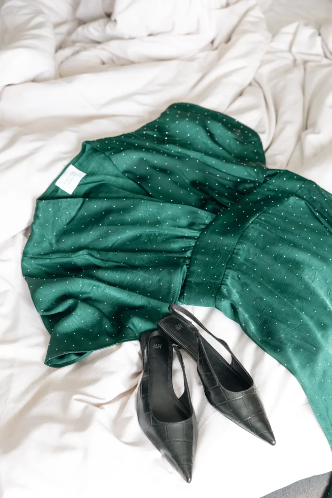 Grön prickig klänning och svarta klackskor arrangerade på vita sängkläder, perfekt för en elegant spa-middag