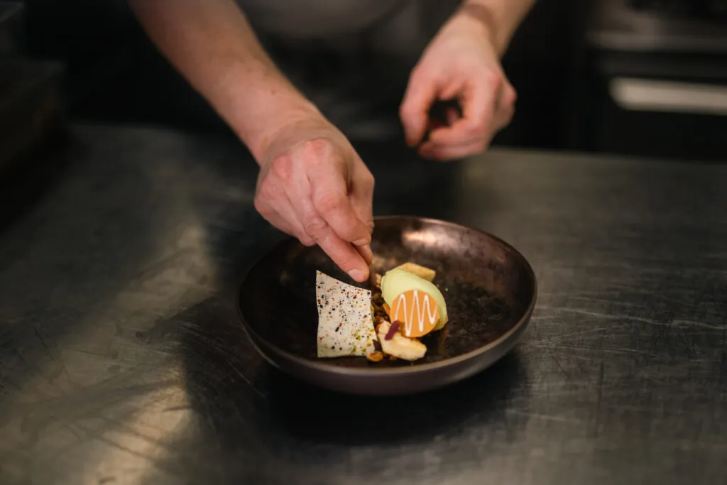 Kock garnerar elegant dessert med färsk frukt och choklad på mörk tallrik i restaurangkök