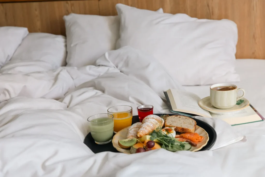 Luxus-Frühstück im Bett mit Kaffee, Saft, Croissants und frischem Obst auf weißer Bettwäsche