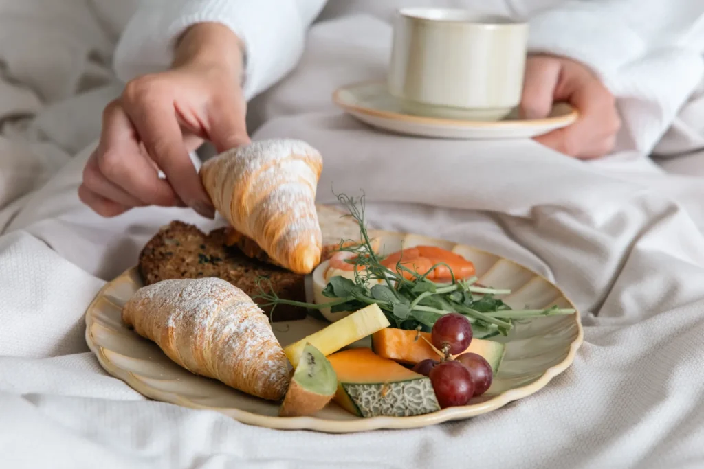 Lyxig frukost på sängen med croissanter, färsk frukt, ost och kaffe serverat på elegant porslin