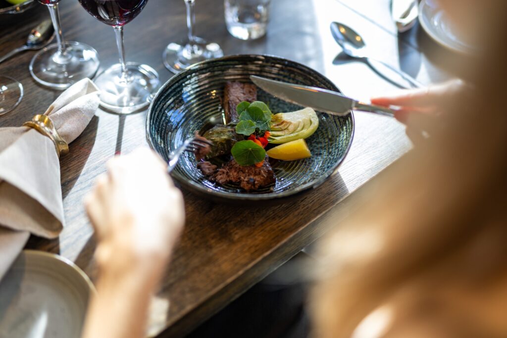 Elegantes Restaurantessen mit Fleisch in einer dunklen Schale, dekoriert mit Gemüse und serviert mit Rotwein auf dem Tisch