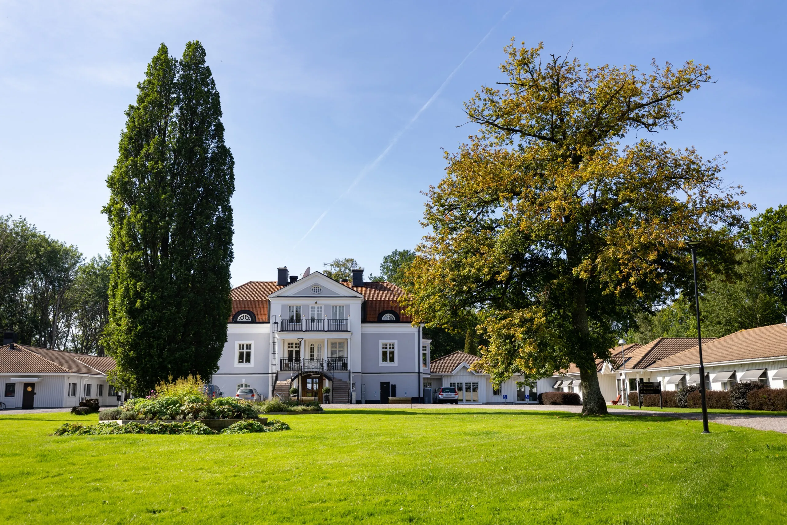 Starby Spa & Hotells huvudbyggnad, en vit herrgård med rött tegeltak omgiven av grönskande park och träd