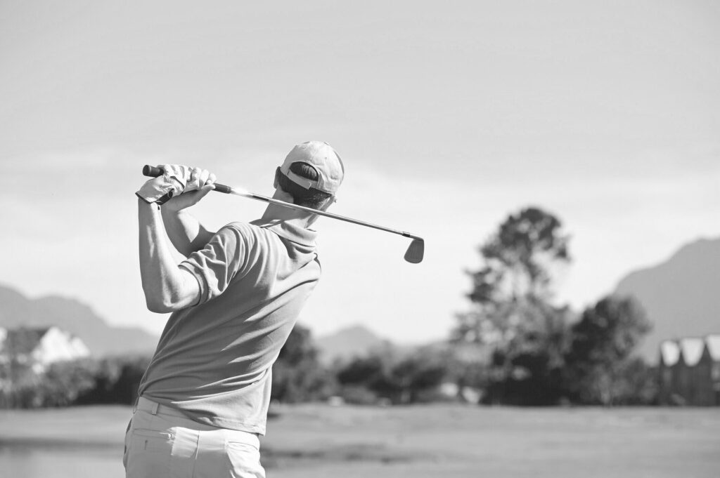 Golfer beim Schwung auf einem Golfplatz mit Bergen und Bäumen im Hintergrund