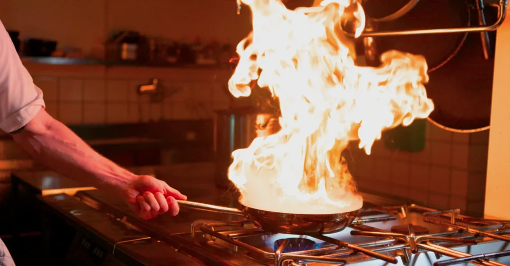Kock flamberar en rätt i stekpanna med höga lågor på restaurangens professionella kök