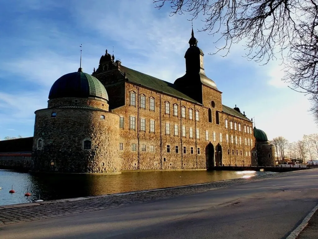 Vadstena slott vid Vättern med rund torn, grön kuppel och stenmurar som speglas i vattnet