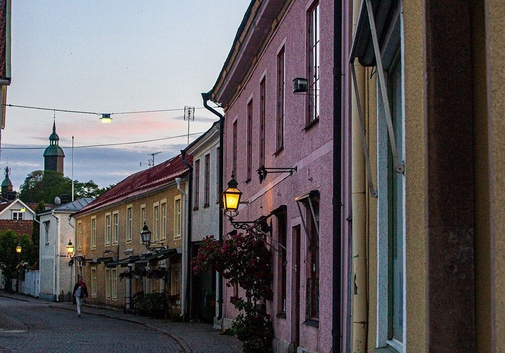 Vadstenas charmiga gamla stan Kullerstensbelagd gata i Vadstenas historiska centrum med färgglada byggnader och kyrktorn i bakgrunden