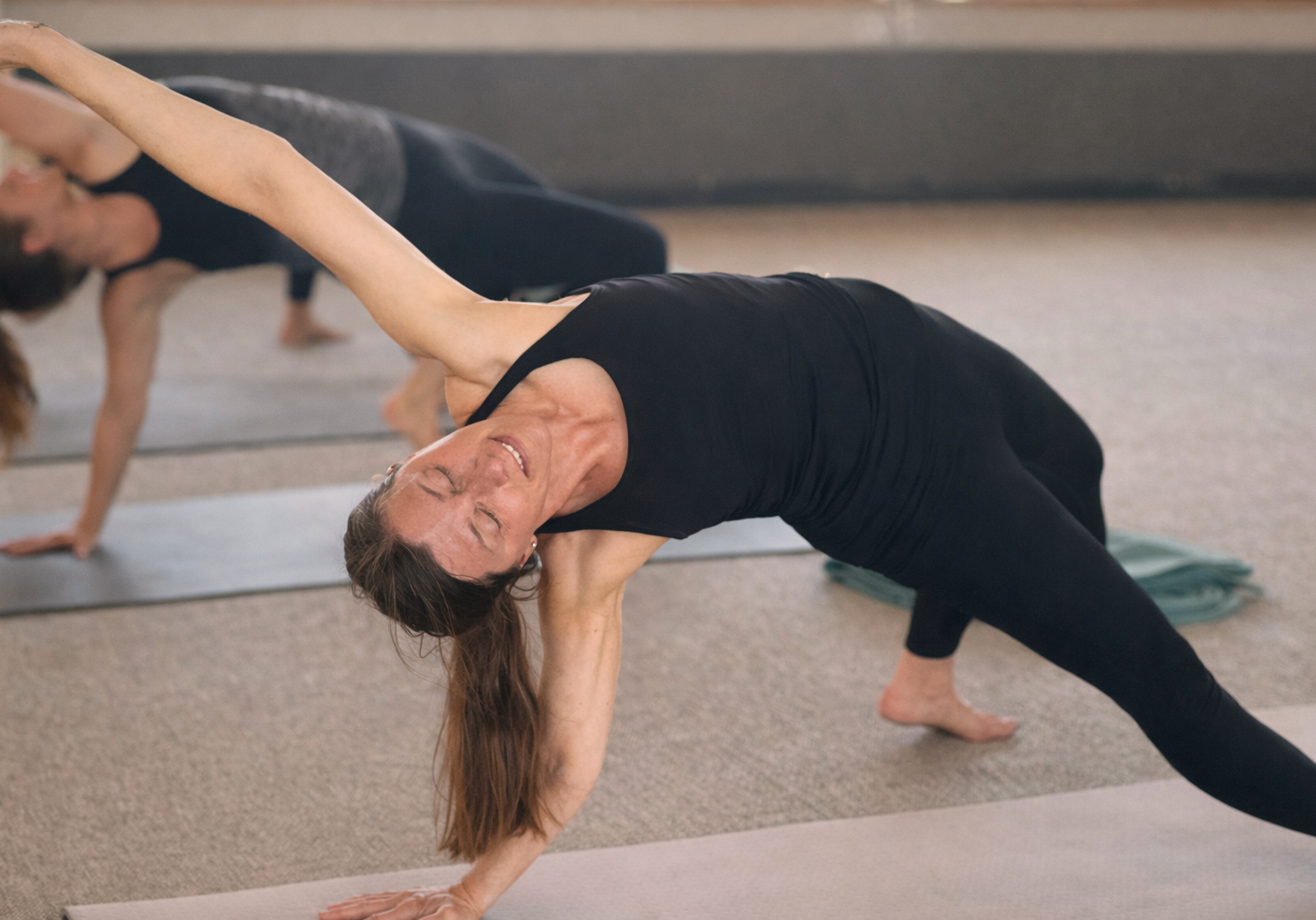 Kvinna i svart träningsoutfit utför sidoplanka i yogaklass på Starby Spa & Hotell